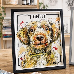 May include: A framed watercolor painting of a curly-haired dog with golden-brown fur, wearing a yellow collar. The artwork features the name TOMMY in black ink at the top, with expressive paint splatters in red and yellow on a white background.