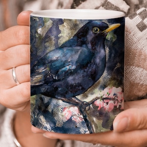 May include: A blackbird with a yellow beak perched on a branch with pink blossoms. The bird is painted in a watercolor style with a blue and green background.