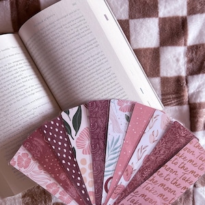 May include: A set of pink and brown patterned bookmarks with floral and geometric designs. The bookmarks feature the text "Take me to the moon" in a cursive font.