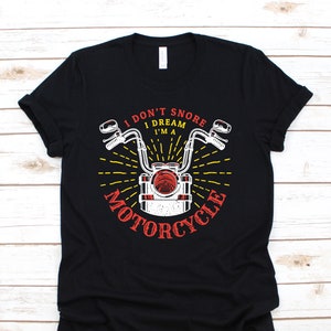 Könnte beinhalten: Schwarzes T-Shirt mit einem Grafikdruck eines Motorrad-Scheinwerfers und Lenkers. Der Text "I don't snore I dream I'm a motorcycle" ist auf dem Shirt aufgedruckt.