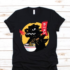May include: Black t-shirt with a cartoon Godzilla eating ramen noodles. The text "Ramen" is written in Japanese on a red banner.
