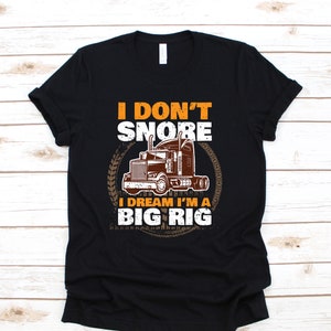 以下が含まれることがあります： 黒いTシャツに、茶色のセミトレーラーのグラフィックと「私はいびきをかかない、私は大型トラックであることを夢見ている」というテキストが書かれている。
