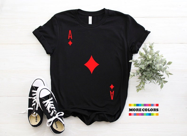 May include: Black t-shirt with a red ace of diamonds playing card graphic. The shirt is laying flat on a white surface. "MORE COLORS" is written in black text on a rainbow stripe background.
