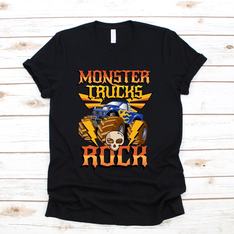 Puede incluir: Camiseta negra con un gr&aacute;fico de un cami&oacute;n monstruo azul con llamas amarillas y el texto "Monster Trucks Rock" en naranja y amarillo.
