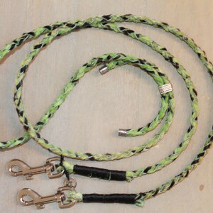 May include: A braided dog leash with black and green accents. The leash has two silver clips and a silver bead.