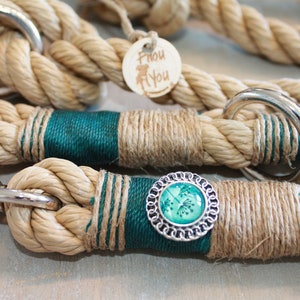 May include: A close-up of a natural rope dog leash with teal blue accents and a silver charm with a green floral design. The leash has a silver clasp and a silver ring.