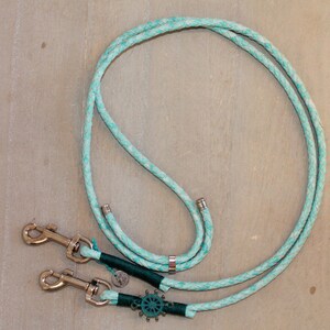 May include: A turquoise blue double dog leash with two silver clips and a silver ring. The leash has a green and silver nautical wheel charm.