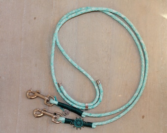 May include: A turquoise blue double dog leash with two silver clips and a silver ring. The leash has a green and silver nautical wheel charm.