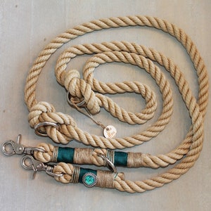 May include: A natural-colored rope dog leash with two green and gold accents and two silver clips. The leash is coiled on a light gray surface.