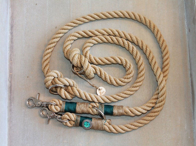 May include: A natural-colored rope dog leash with two green and gold accents and two silver clips. The leash is coiled on a light gray surface.