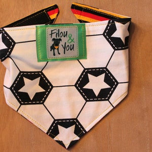 May include: A white and black soccer ball patterned dog bandana with yellow stitching. The bandana has a green label with the text "Filou & You" and a black silhouette of a dog wearing a yellow collar.