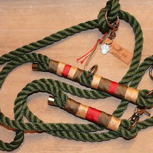 Op de afbeelding: Groene touwhalster voor honden met rode en bruine accenten. De halster heeft twee clips en een klein sieraad met een pootprint en de tekst "Treat You" op een houten label.