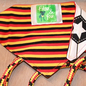 May include: A red, yellow, and black striped dog bandana with a white soccer ball design and a green label that says "Filou & You".
