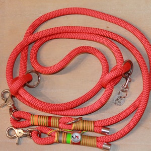 Könnte beinhalten: Eine rote Hundeleine aus Seil mit zwei Clips und einem Metallring. Die Leine hat an einem Ende ein buntes Streifenmuster.