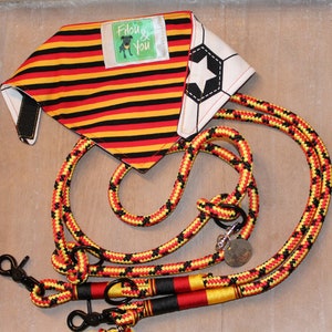 May include: A red, yellow, and black striped dog bandana with a white soccer ball design and a black and white dog silhouette logo that says "Fidoug & You". The bandana is paired with a red, yellow, and black rope dog leash with two clips.