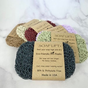 May include: Five colourful soap lift pads made of eco-friendly bio plastic. The pads are designed to keep soap bars elevated and dry, extending their lifespan. The packaging features the brand name "SOAP LIFT" and the text "Rest your soap high and dry" and "Eco Friendly bio Plastic".