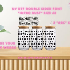 May include: Three clear glass tumblers with bamboo lids and straws are displayed on a wooden surface. Each tumbler is printed with a black and white alphabet design. The text "UV DTF DOUBLE SIDED FONT" and "INTRO RUST" are visible.