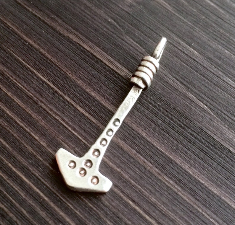 May include: A silver pendant in the shape of a hammer with a decorative, twisted wire loop at the top.