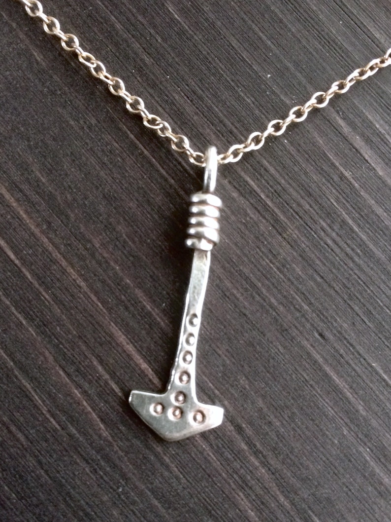 May include: A silver necklace with a hammer pendant. The hammer has a textured surface and a rounded top.