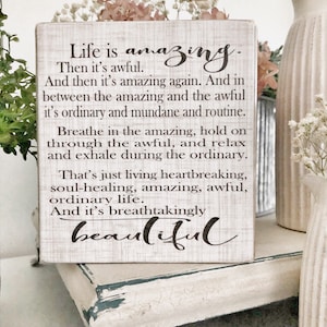 May include: White wooden sign with black text that reads "Life is amazing. Then it's awful. And then it's amazing again. And in between the amazing and the awful it's ordinary and mundane and routine. Breathe in the amazing, hold on through the awful, and relax and exhale during the ordinary. That's just living heartbreaking, soul-healing, amazing, awful, ordinary life. And it's breathtakingly beautiful."