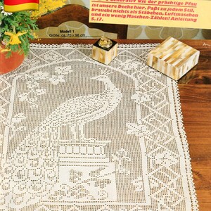 May include: Cream-colored, crocheted peacock tablecloth, approximately 27.5 x 38.5 inches, with a detailed peacock design in the center and a decorative border. The image includes a German flag and text in German.