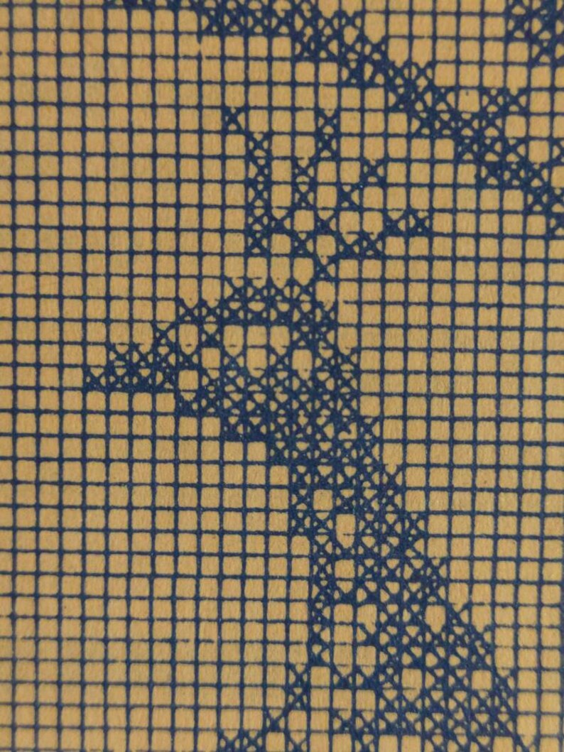 May include: Close-up of a tan paper with a blue grid pattern. A blue, abstract design is overlaid on the grid, creating a textured effect. The design appears to be a stylized representation of a natural form.