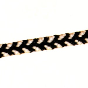 Peut inclure: Une sangle de guitare noire et crème avec un motif en chevrons. La sangle est faite d'un matériau tissé. La sangle est conçue pour être portée sur l'épaule et convient aux guitares acoustiques ou électriques.