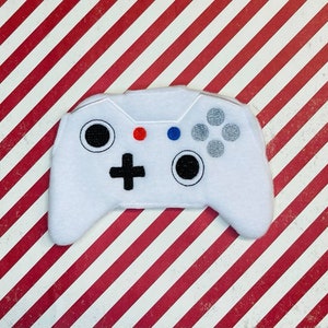 May include: White plush toy shaped like a video game controller. The controller has black buttons and a black directional pad.