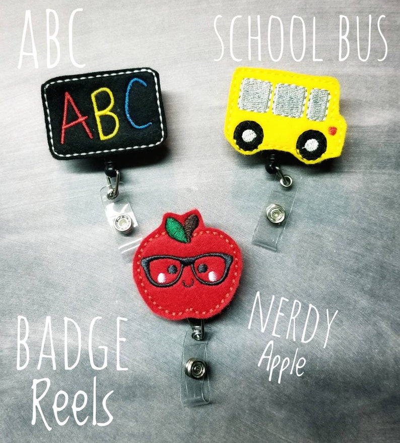 May include: Three badge reels with school-themed designs. One is a black rectangle with "ABC" in colorful letters, another is a yellow school bus, and the last is a red apple wearing glasses. The words "Badge Reels" and "Nerdy Apple" are also visible.