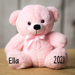 Pu&ograve; includere: Un orsacchiotto di peluche rosa con un fiocco rosa. L'orso ha il nome "Ella" scritto su una zampa e l'anno "2021" scritto sull'altra zampa.