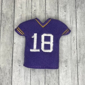 May include: Purple felt football jersey with yellow trim and the number 18 in white.