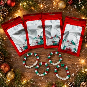 May include: Four red and silver foil pouches containing beaded bracelets with white labels reading Becca, Clay, Addison, and Tristan. Below the pouches are four circular beaded bracelets in red, white, and green with letter beads spelling names.