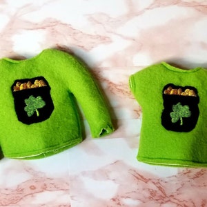 May include: Two green felt shirts with a gold pot of coins and a shamrock design. The larger shirt has long sleeves and the smaller shirt has short sleeves.