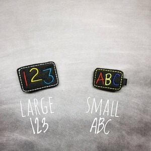 May include: Two black felt patches with white stitching. One patch has the numbers 123 in red, yellow, and blue. The other patch has the letters ABC in red, yellow, and blue. The text "LARGE 123" and "SMALL ABC" are below the patches.