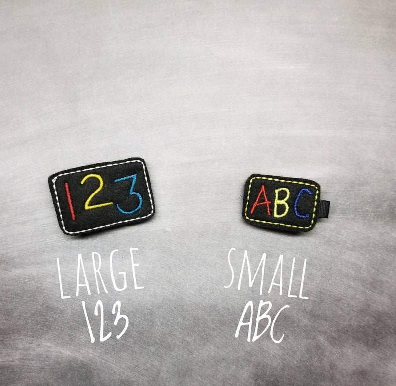 May include: Two black felt patches with white stitching. One patch has the numbers 123 in red, yellow, and blue. The other patch has the letters ABC in red, yellow, and blue. The text "LARGE 123" and "SMALL ABC" are below the patches.