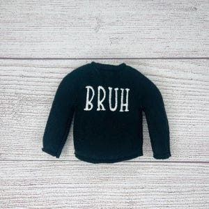 May include: A black long-sleeved shirt with the word "BRUH" embroidered in white on the front.