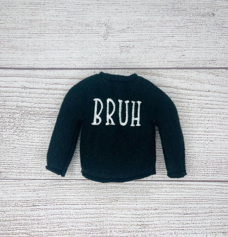 May include: A black long-sleeved shirt with the word "BRUH" embroidered in white on the front.