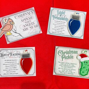 K&ouml;nnte beinhalten: Vier rechteckige Karten mit gestickten Ornamenten: ein roter Kardinal mit dem Text Cardinals Appear When Angels Are Near, eine blaue Gl&uuml;hbirne mit Light of Friendship, eine rote Gl&uuml;hbirne mit Light of Teaching und eine Gew&uuml;rzgurke mit Christmas Pickle.