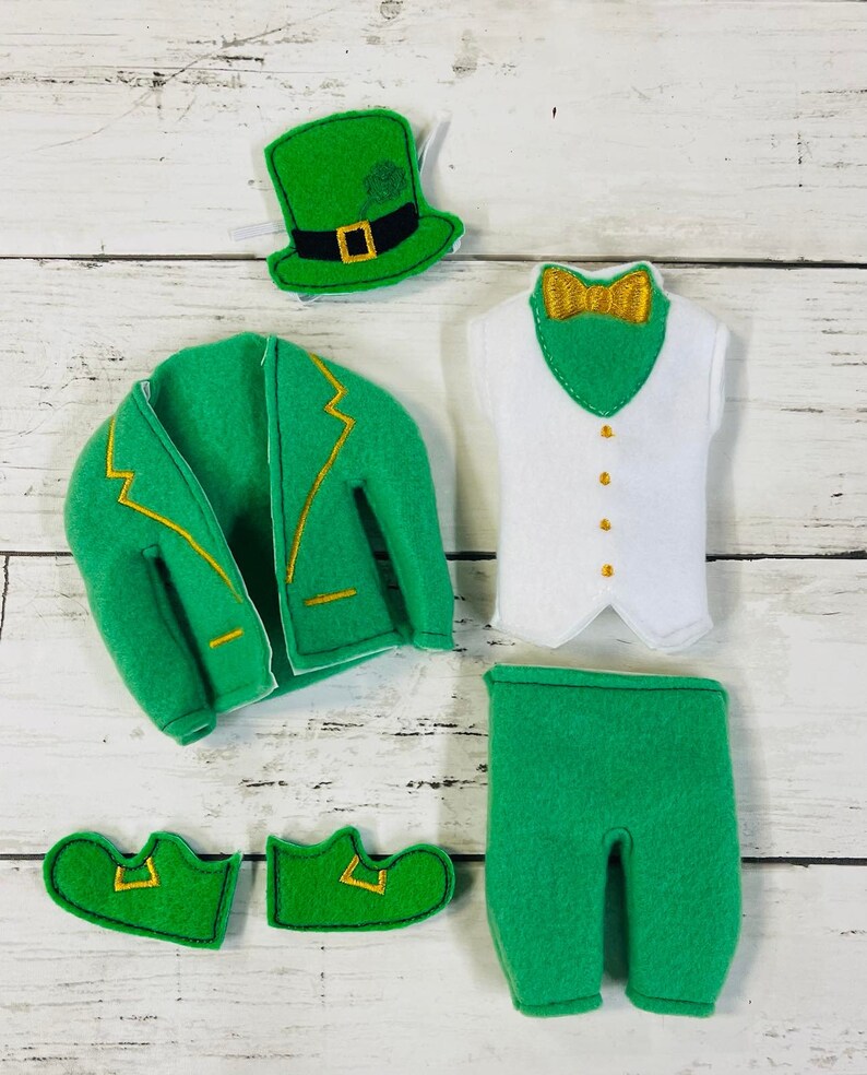 May include: A green felt elf costume with a green hat, white vest, green pants, and green shoes. The hat has a gold buckle and a shamrock on top. The vest has a gold bow tie. The pants have a gold trim. The shoes have a gold buckle.