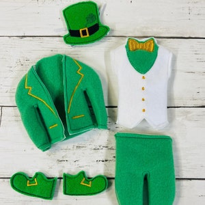 May include: A green felt elf costume with a green hat, white vest, green pants, and green shoes. The hat has a gold buckle and a shamrock on top. The vest has a gold bow tie. The pants have a gold trim. The shoes have a gold buckle.