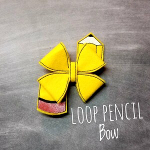 May include: A yellow felt hair bow in the shape of a pencil, with black stitching and a red eraser. The bow is labeled "LOOP PENCIL BOW" in white script on a gray background.