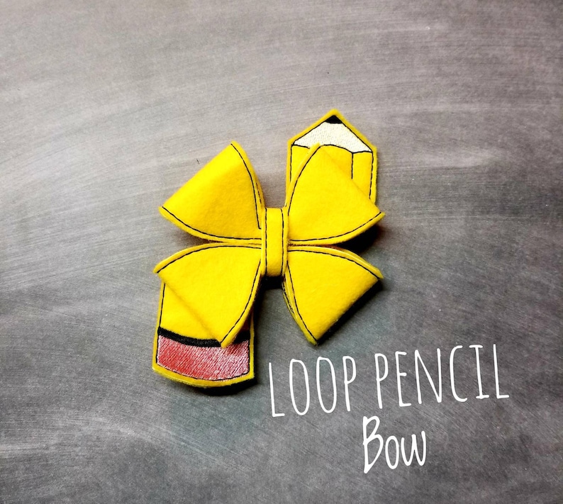 May include: A yellow felt hair bow in the shape of a pencil, with black stitching and a red eraser. The bow is labeled "LOOP PENCIL BOW" in white script on a gray background.
