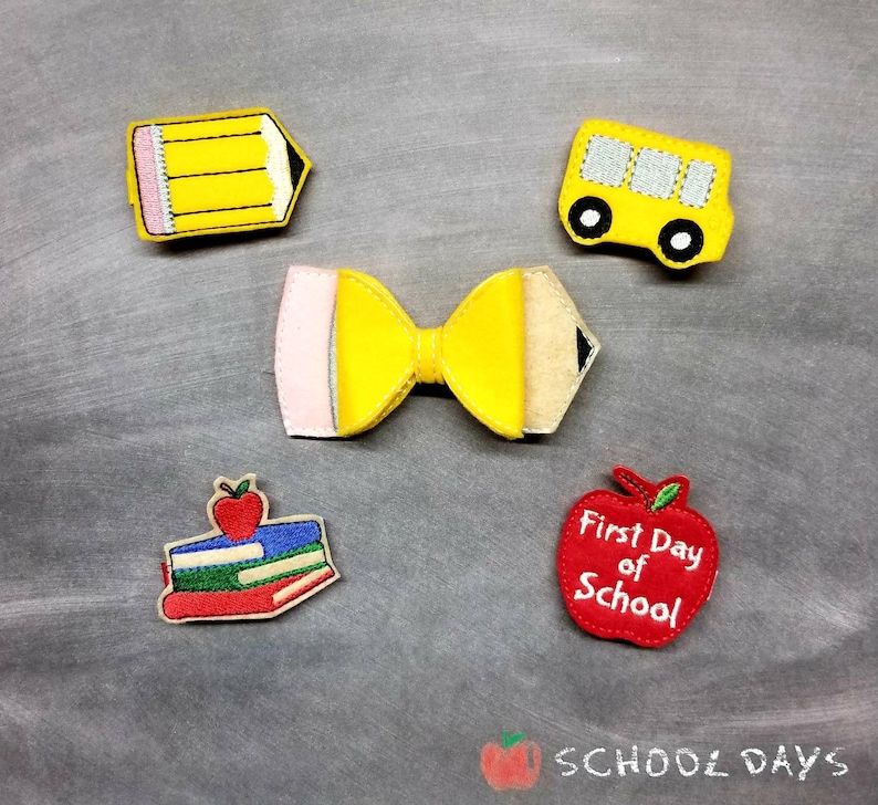 May include: A collection of felt school-themed embellishments, including a yellow pencil, a yellow school bus, a bow shaped like a pencil, a stack of books with an apple, and a red apple with the text "First Day of School".