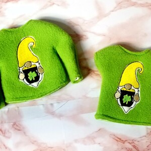 May include: Two green fleece shirts with a gnome holding a pot of gold and a shamrock embroidered on the front. The shirt on the left has long sleeves and the shirt on the right has short sleeves.