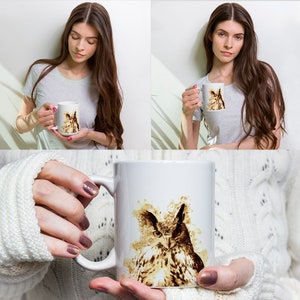May include: White ceramic mug featuring a watercolor-style illustration of an owl in shades of brown and beige. The owl's detailed eyes and feathers are prominent. The mug is held by a person.