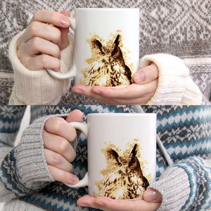 May include: White ceramic mug featuring a watercolor-style illustration of an owl. The owl is depicted in shades of brown and tan, with a detailed rendering of its feathers and facial features. The mug has a standard handle and a glossy finish.