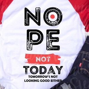 May include: A white raglan shirt with red sleeves. The shirt displays the words "NOPE NOT TODAY" in black block letters, with "TOMORROW'S NOT LOOKING GOOD EITHER" printed below. Dark wash jeans and grey trainers are also visible in the image.