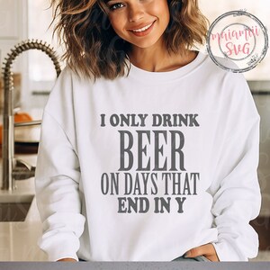 May include: A white long-sleeve crewneck sweatshirt featuring the dark grey text I ONLY DRINK BEER ON DAYS THAT END IN Y printed in a bold, centred font on the chest. The garment has a classic fit with ribbed cuffs and a ribbed neckline.