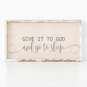 May include: A rectangular framed sign with the text "GIVE IT TO GOD and go to sleep" in black script. The background is a light beige colour, and the frame is white with a distressed finish.