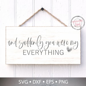 Könnte beinhalten: Ein rechteckiges Holzschild mit dem Schriftzug "and suddenly you were my EVERYTHING" in schwarzer Schrift. Neben dem Wort "my" befindet sich eine kleine Herzgrafik. Das Schild ist weiß und hat eine Seilaufhängung.